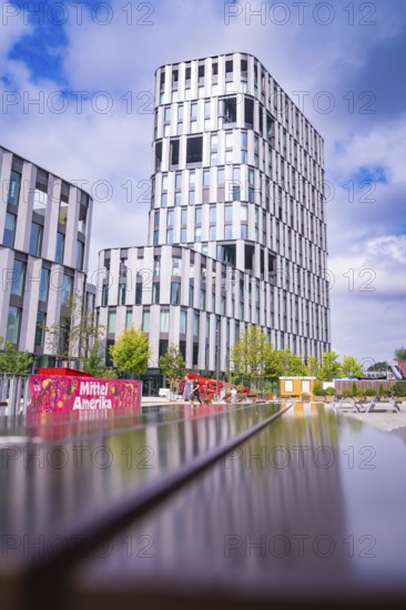 Futuristic high-rise building and park landscape under a blue sky with a colourful element, Munich, Germany