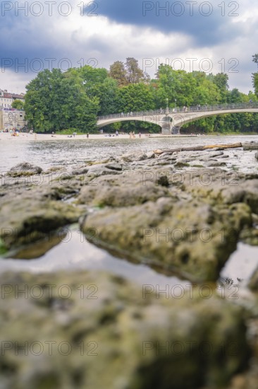 River landscape with bridge and trees, cloudy sky and stony shore area, Munich, Germany