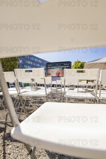 White chairs arranged in rows with a view of a screen and a building in the background, open air cinema Sindelfingen, district of böblingen, Germany