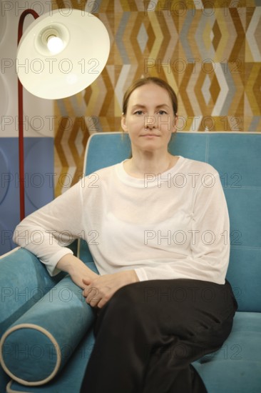 A woman relaxes on a vibrant blue sofa, surrounded by decorative walls featuring geometric patterns. Natural light fills the room, creating a warm and inviting atmosphere for her serene expression