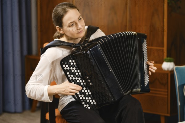 A middle-aged woman concentrates as she plays the accordion in a warmly decorated room, creating a serene atmosphere filled with music. The setting enhances the intimate vibe of her performance
