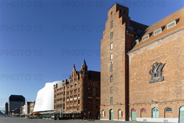 At the front right silo IV, built 1935-36, on windowless wall stylised relief of a cog, behind it turreted warehouse built 1905 and warehouse II built 1888, brick building, in front of it open-air seating, restaurant, behind it Ozeaneum, at the very back silo III, Hafenstraße, harbour island, Old Town, UNESCO World Heritage Site, Hanseatic City of Stralsund, Mecklenburg-Western Pomerania, Germany
