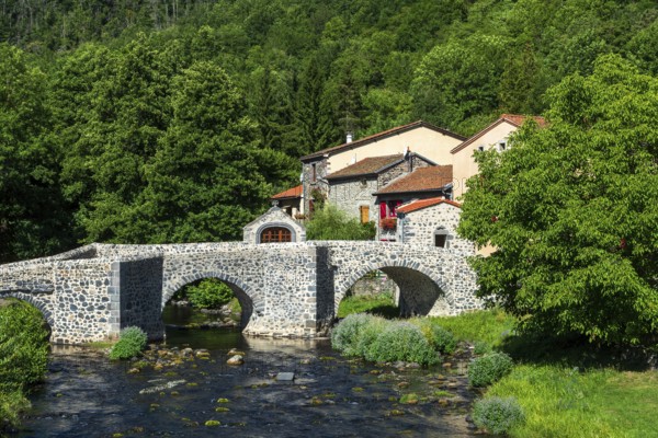 Stone bridge over the Pavin couze river flowing through the village of Saurier, Puy de Dome. Auvergne Rhone Alpes, France