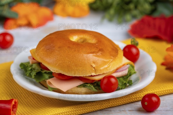 A filled bagel on a plate, decorated with tomatoes on a yellow cloth