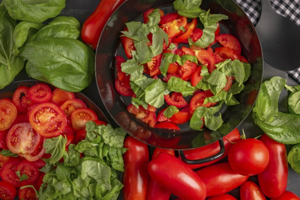 A pan filled with sliced tomatoes and basil leaves, surrounded by fresh vegetables