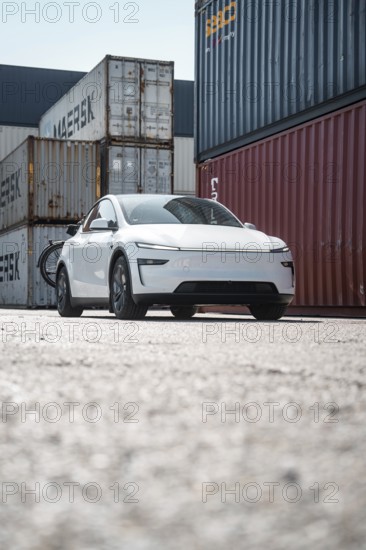 White car in a container port with different coloured freight containers, Tesla Model Y Juniper, electric car