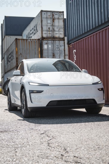 Modern white car in an industrial area surrounded by freight containers, Tesla Model Y Juniper, electric car