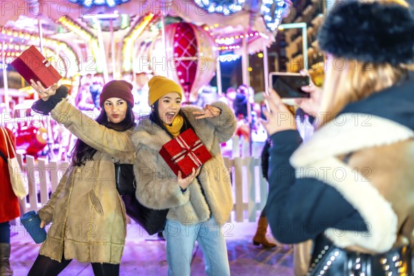 Three happy women posing with christmas gifts in front of carousel at night in a christmas market