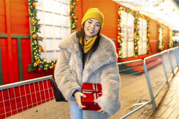 Happy young woman holding christmas gift while visiting a decorated christmas market at night