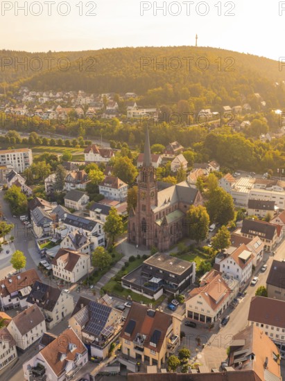 View of a church with surrounding houses and a background of wooded hills in golden light, small town of Perle Nagold, Black Forest, Germany