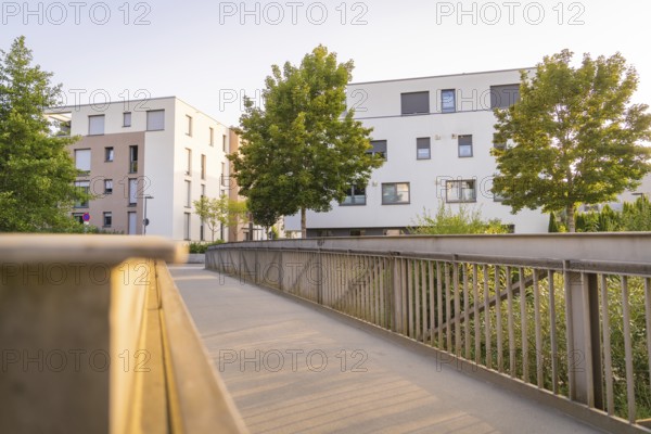 Modern residential buildings and trees flanking a bridge in the evening sun, small town of Perle Nagold, Black Forest, Germany