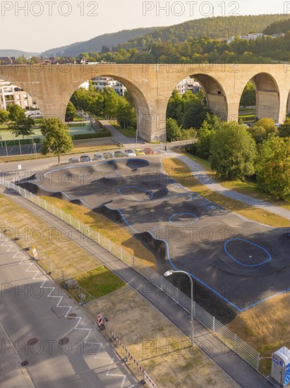 A pump track with asphalt and blue lines under a bridge in a green urban landscape, pump track, Nagold, Black Forest, Germany