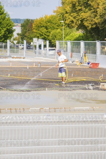 Construction worker watering concrete on a building site, surrounded by safety fences, car park construction, Calw, Germany