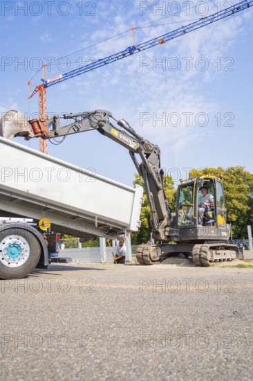 Excavator loading materials into a lorry on a construction site under a clear sky, car park construction, Calw, Germany