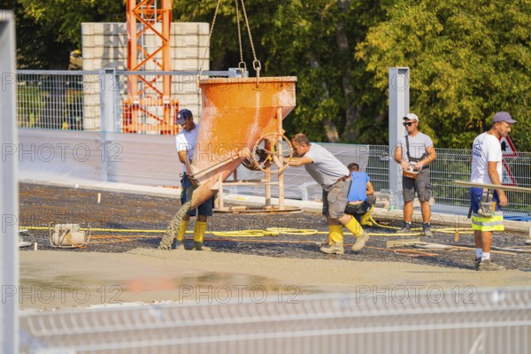 Workers pouring concrete with a shaking bucket on a sunny construction site, car park construction, Calw, Germany