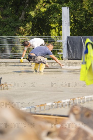 Workers bend over a concrete surface and use tools on a construction site, car park construction, Calw, Germany