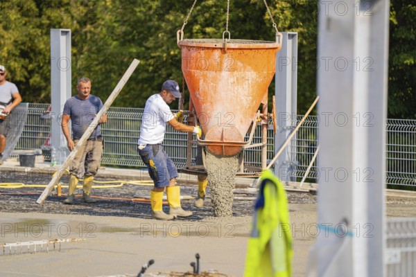 Construction workers unloading concrete with a large hopper on a building site with metal structures, car park construction, Calw, Germany
