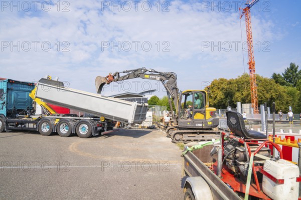 Excavator working on loading a lorry on a construction site, cranes in the background, car park construction, Calw, Germany