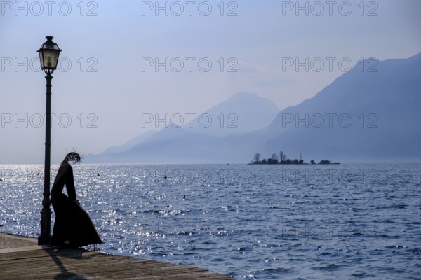 Sculpture of a fisherwoman at the harbour of Cassone di Malcesine, in the background Isole di Trimelone, Lake Garda, Veneto, Italy