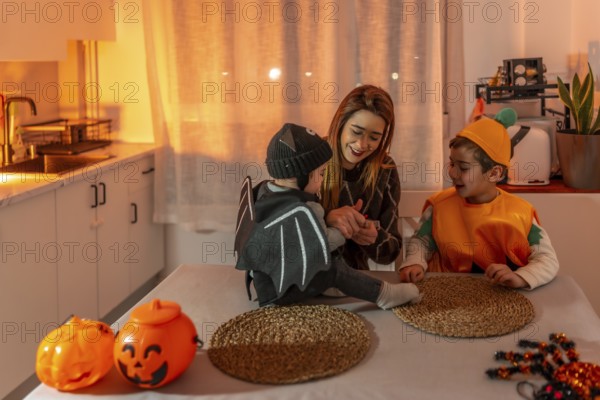 Mother and children wearing halloween costumes are sitting at a table in the kitchen, playing and smiling