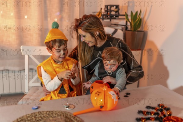 Mother and children with painted faces wearing halloween costumes are playing at home with pumpkin bucket and candies