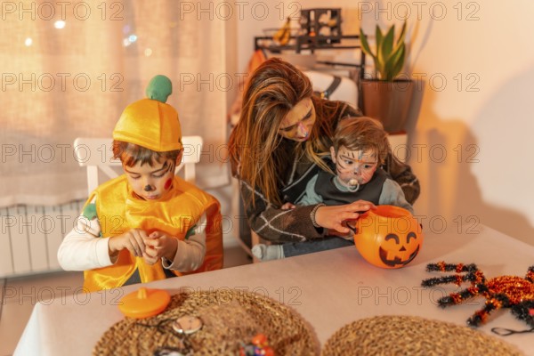 Mother and children wearing festive halloween costumes, joyfully preparing treats together at home, surrounded by autumn decorations and candy