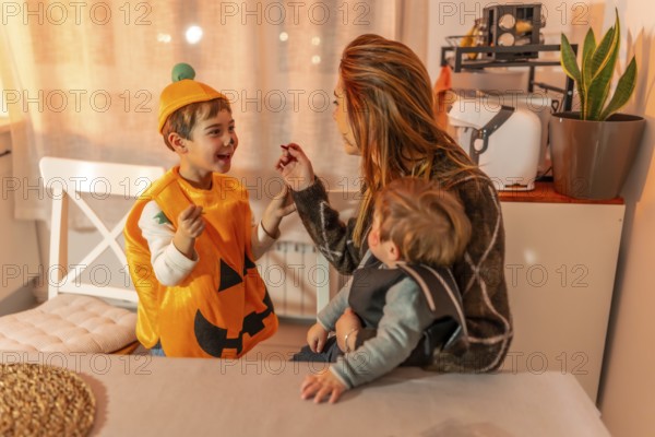 Mom applying halloween makeup on her kid's face, while holding her baby, preparing for trick or treating