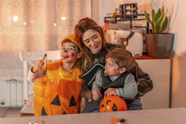 Mom and her kids are smiling, wearing halloween costumes and makeup, holding pumpkin buckets and having fun at home