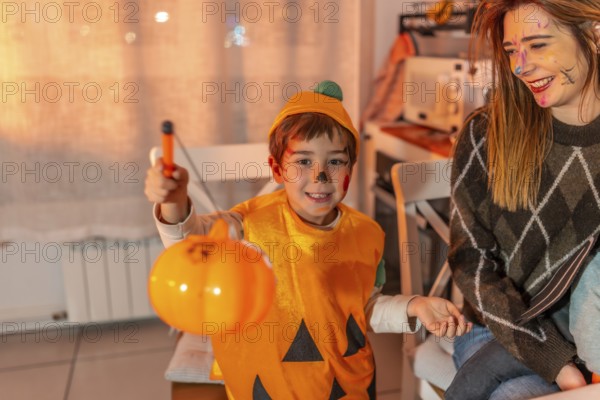 Happy child wearing pumpkin costume holding a plastic jack o' lantern celebrating halloween with family at home