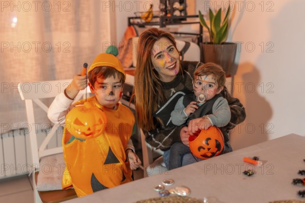 Mother and children with painted faces are smiling and holding pumpkin buckets, celebrating halloween at home