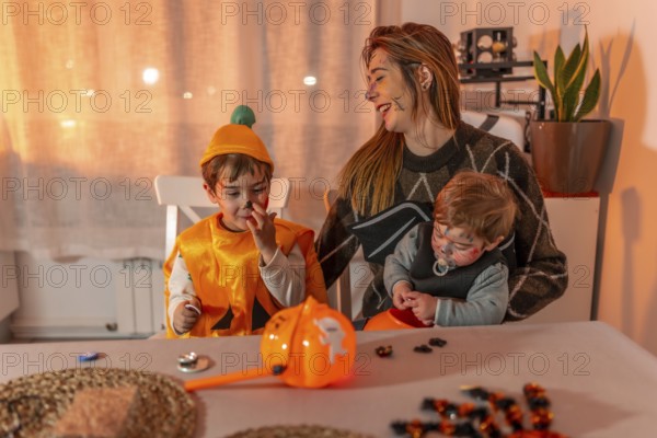 Mother and her two children wearing halloween costumes and makeup, playing with candies on a table at home