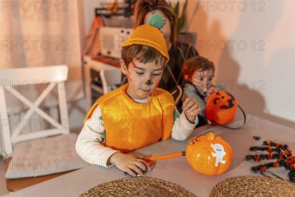 Children with painted faces preparing halloween pumpkin decorations at home, with their mother dressed up in the background