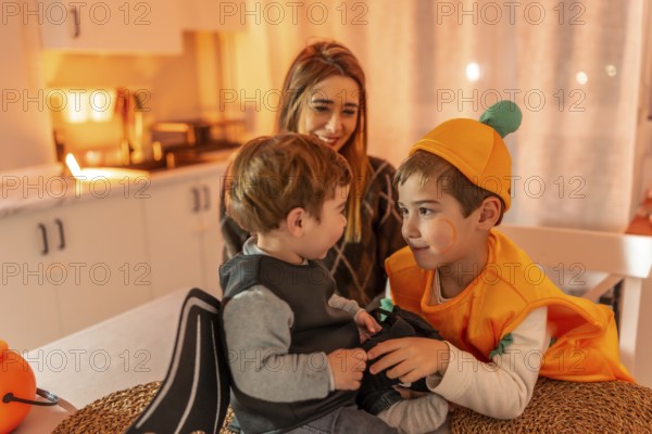 Two young brothers wearing halloween costumes playing together at home, watched by their smiling mother