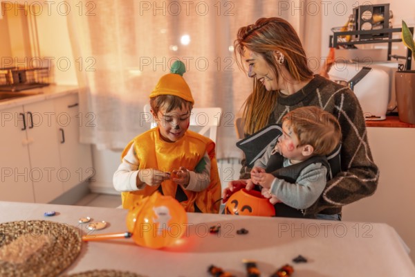 Mother and children wearing halloween costumes are sitting at the kitchen table and preparing for trick or treat