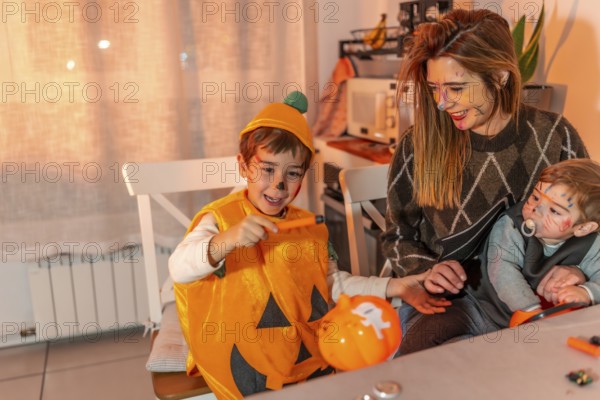 Happy children with painted faces wearing halloween costumes painting pumpkins with their mother at home