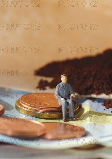 Miniature figure of a man sitting on coins and banknotes, ground coffee in a filter bag in the background, North Rhine-Westphalia, Germany