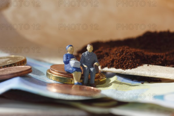 Miniature figure of a married couple sitting on coins and banknotes, ground coffee in a filter bag in the background, North Rhine-Westphalia, Germany