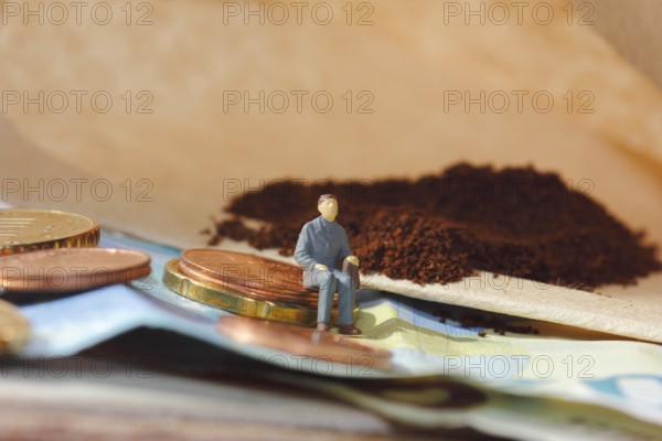 Miniature figure of a man sitting on coins and banknotes, ground coffee in a filter bag in the background, North Rhine-Westphalia, Germany