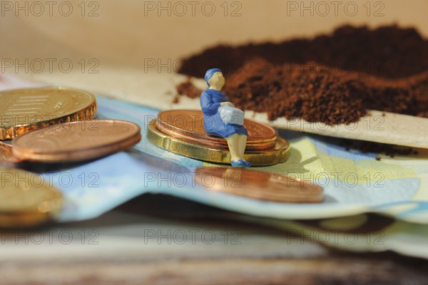 Miniature figure of a woman sitting on coins and banknotes, ground coffee in a filter bag in the background, North Rhine-Westphalia, Germany