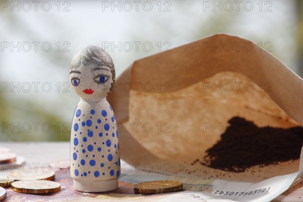 Pretty female wooden cone figure with coins and banknote in front of filter bag with coffee North Rhine-Westphalia, Germany