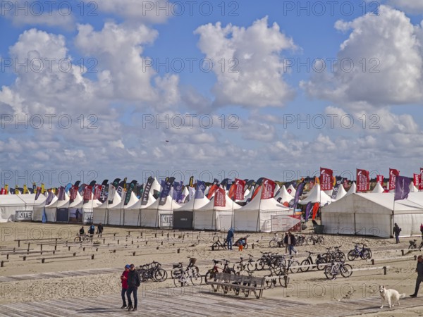 California kitesurfing Masters 2025, Kite Village tents with kite equipment for sale, marketplace, try out, kitesurfing on the North Sea beach, blue sky, sun, summer, flags, bicycles, Ording, Sankt Peter-Ording, Schleswig-Holstein, Germany