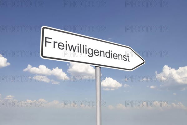 (Photomontage) Directional arrow with the inscription FREIWILLIGENDIENST against a blue sky