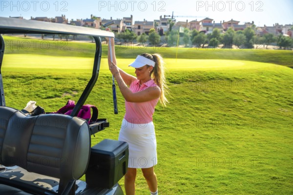 Female golfer placing her golf club into the cart while enjoying a sunny day on a lush green golf course, embracing leisure and sport