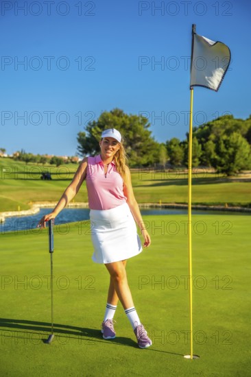 Female golfer standing confidently near the hole, holding her putter on a sunny day at the golf course, enjoying the outdoor leisure activity