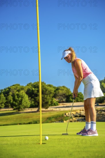 Professional golfer concentrating on the green, about to putt during a sunny day on a beautiful golf course