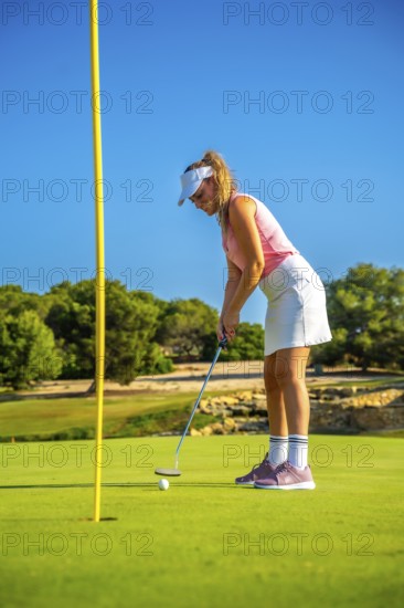 Professional golfer putting a ball on the green under the bright sun, enjoying a beautiful day on a picturesque golf course
