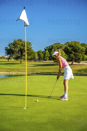 Female golf player putting the ball on the green under a bright sun, showcasing skill and concentration in a vibrant outdoor setting