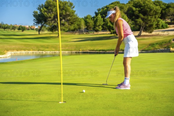 Professional golfer putting the ball on a sunny day, enjoying the beautiful scenery of a lush golf course surrounded by nature