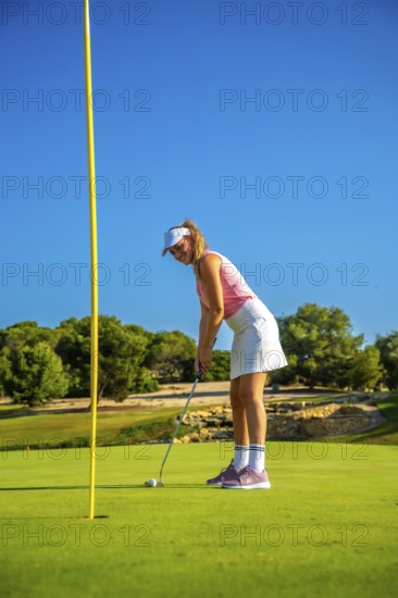 Female golfer putting the ball on the green under a bright sun, showcasing skill and precision on the lush course during summer