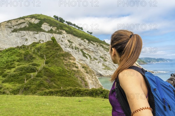 Female tourist with backpack admiring the coastal landscape of sakoneta beach and its flysch cliffs, a unique geological formation in zumaia, basque country